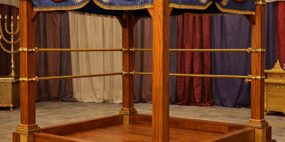 Wooden canopy bed frame with red and blue draped fabric and gold trim