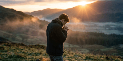 Man kneeling on blanket outdoors praying at sunrise in valley