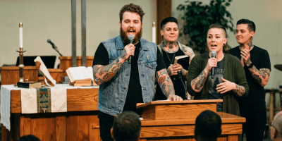 Four tattooed worship leaders singing and speaking before a congregation in church